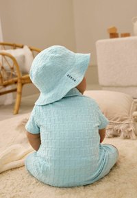 Conjunto de algodón texturizado en azul claro con mangas cortas y sombrero de cubo a juego, que presenta un patrón sutil y una etiqueta de marca en el sombrero.