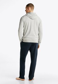 Sudadera gris de manga larga con capucha ajustable; combinada con pantalones sueltos, de color marino. El material parece suave, elástico y cómodo.