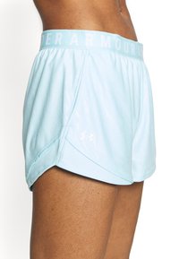 Vaaleansiniset urheilushortsit, joissa on joustava vyötärönauha ja vaaleansininen "UNDER ARMOUR" -logo. Sileä kangas, jossa on kevyt kiilto ja sivuhaarat.