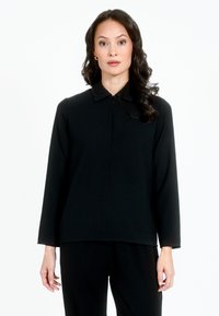 Juodas ilgomis rankovėmis viršus su apykakle, pasižymintis užtrauktuko uždarymu ir lygiu, tekstūruotu audiniu. Paprasta, tiesi forma ir minimalus dizainas.