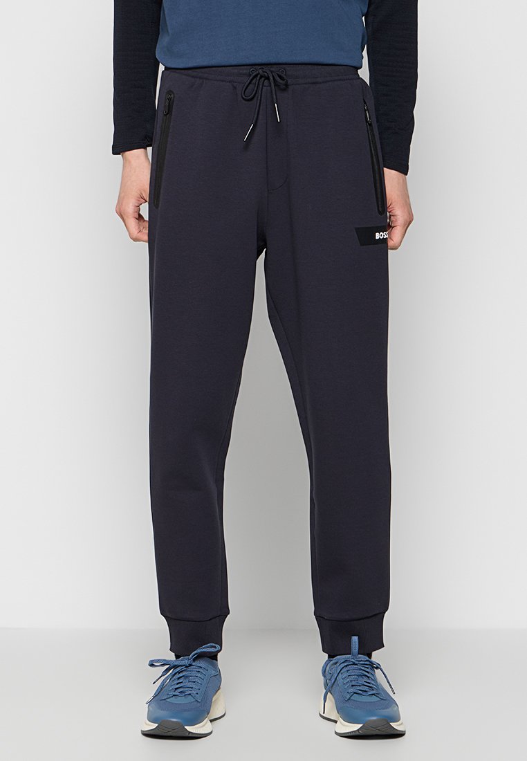 Marineblauwe sweats met een koord in de taille, taps toelopende benen, ritszakken aan de zijkant en een logopatch op de linker dij.