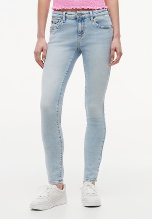 Blugi din denim albastru deschis, slim-fit, purtați cu adidași albi și un top roz scurt, văzuți de la talie până la picioare.