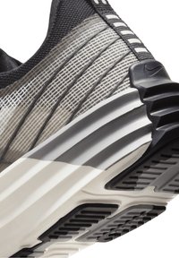 Svart och grå atletisk sko med texturerad ovandel, distinkt randigt mönster och en vadderad sula med räfflad svart gummisula.