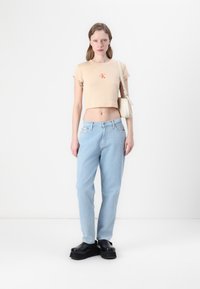 Licht perzik geknipte t-shirt met "CK" logo, lichtblauwe rechte jeans en zwarte platform schoenen. Minimalistische witte handtas.