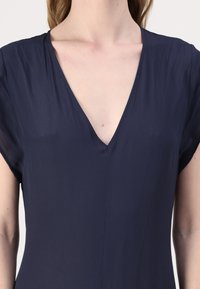 Námořnickomodré šaty s výstřihem do V a krátkými rukávy, s hladkou texturou a minimalistickým designem, ideální na vrstvení nebo na běžné nošení.