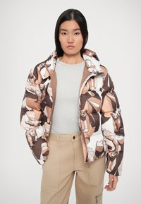 Giubbotto imbottito con un motivo geometrico di orso in tonalità marrone e bianco, dotato di cappuccio, chiusura con zip e texture trapuntata.