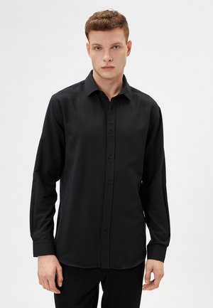 Camisa negra de manga larga con cierre de botones en la parte delantera, cuello clásico y textura suave. Presenta un corte ajustado y puños con un solo botón.
