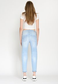 Ljusblå skinny jeans med fransar nertill, femficksdesign och subtila blekningar, bärs med en kort vit topp och sneakers.