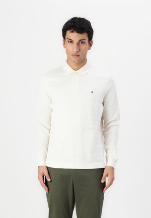 Polo à manches longues en crème avec de légères rayures tonales, col boutonné et petit logo sur la poitrine. Texture en coton.
