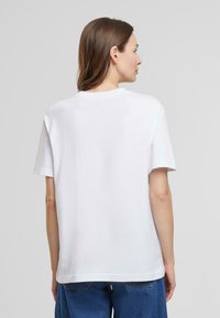 White cotton t-shirt with short sleeves, crew neckline, straight hem, and a relaxed fit, shown from the back against a grey background.