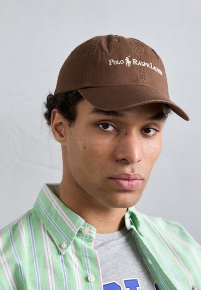 Svetlo rjava bejzbolska kapa z belim logotipom "Polo Ralph Lauren" spredaj. Ima strukturno obliko in gladko teksturo tkanine.