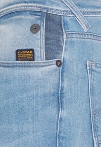 Vaqueros de mezclilla azul claro con un acabado desgastado, que presentan un botón negro, acentos de costura y una etiqueta que dice "G-Star RAW."