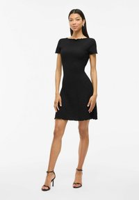 Vestido negro de manga corta con tejido texturizado, corsé ajustado y falda acampanada. Escote y dobladillo con forma de onda. Llega por encima de la rodilla.