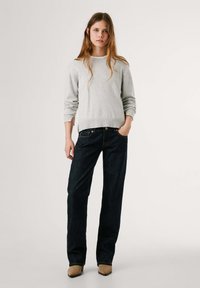 Maglione in misto lana grigio chiaro con collo a giro, abbinato a jeans in denim blue scuro. I jeans presentano cinque tasche e dettagli di cucitura a contrasto.