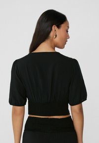 Top corto negro con mangas abullonadas y cinturilla fruncida. Tejido suave, detalles de costura mínimos y escote redondeado.