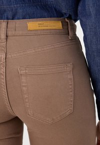 Jeans en denim marron avec une coupe slim, dotés d'une poche arrière et d'une étiquette jaune avec le texte "ONLY". La texture semble lisse et légèrement extensible.