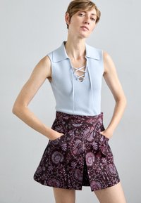 Világoskék, bordázott, ujjatlan felső, fűzős részletekkel; sötét szoknya virágmintával, oldalsó zsebekkel és bővülő fazonnal.