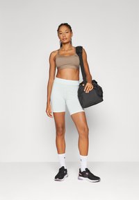 Light blue moisture-wicking shorts, brown sports bra, black training shoes with pink accents, and a black gym bag. White athletic socks.