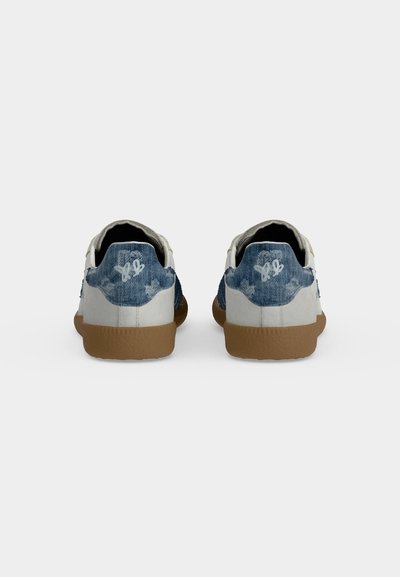 Paire de baskets blanches et bleues avec semelles en gomme vues de dos sur un fond gris uni.