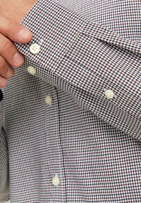 Rutigt knapp-up skjorta i vitt, rött och marinblått. Har pärlknappar, en manschett med en liten öppning och ett texturerat tygmönster.