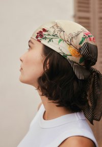 Pañuelo de seda con patrones florales en rojo, amarillo y verde, con un detalle de cinta a rayas en blanco y negro en un lado.