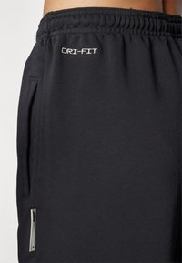 Černé šortky DRI-FIT s elastickým pasem, bočními kapsami, hladkým povrchem a malým stříbrným logem Nike na boku.