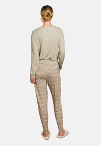 Langärmliges, hellgraues Oberteil mit strukturiertem Muster, kombiniert mit gemusterten, taillierten Hosen in Beige, die florale Designs in Rot und Grün aufweisen.