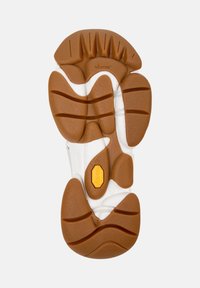 Suela de goma marrón con diversos patrones de pisada, mostrando el logo de Vibram y un distintivo emblema amarillo, diseñado para proporcionar agarre y soporte.