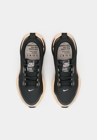 Baskets de course noires avec un dessus texturé, accents beige clair sur la semelle et lacets noirs. Présente un logo et des détails réfléchissants.