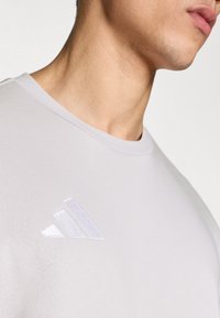 Ανοιχτό γκρι κοντομάνικο μπλουζάκι με απαλή υφή, με λευκό κεντημένο λογότυπο adidas στο επάνω αριστερό μέρος.