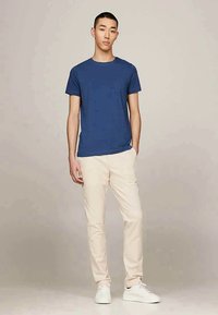 Tumši zilas krāsas kokvilnas t-krekls ar apaļu kakla izgriezumu, pārī ar krēmbaltiem biksēm. Modelis valkā baltas sporta apavus. Vienkāršs un klasiskas dizains.