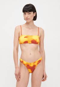 Bikini v rumeno-in-oranžni tkanini s spiralnim vzorcem in rebrasto teksturo, ki vključuje bandeau vrh in hlačke z visokim pasom ter tankimi naramnicami.