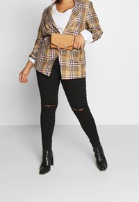 Plaid blazer in earthy tones, paired with a white top, black ripped skinny jeans, and black heeled boots. Brown belt bag accent.