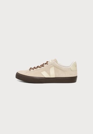 Baskets basses beige en daim avec semelle marron foncé, logo crème "V" sur le côté, et lacets marron à motifs sur fond blanc.