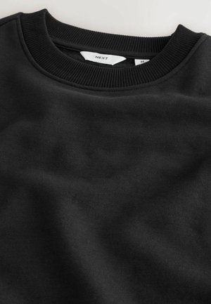 Sort sweatshirt med ribbet rund halsudskæring. Blødt, tekstureret stof med en glat finish. Etiket viser mærket "NEXT" og størrelse "M."