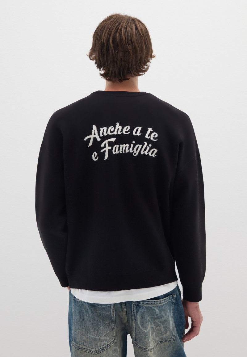 Maglione nero con maniche lunghe e colletto a giro. Sul retro è presente testo ricamato bianco "Anche a te e Famiglia." Texture morbida, vestibilità comoda.