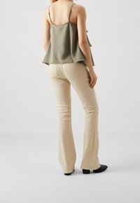 Khaki flared top with a textured finish and layered hem, paired with beige fitted pants, featuring a subtle stretch and classic back pockets.