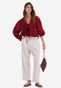 Rød blomstermonstreret cropped top med puffede ærmer, parret med hvide high-waisted bukser og lysebrune flade sko, mens hun bærer en brun taske.