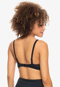 Bralette nera a costine con spalline regolabili, chiusura con ganci e occhielli e design sagomato per una vestibilità aderente. Il tessuto testurizzato offre una leggera lucentezza.