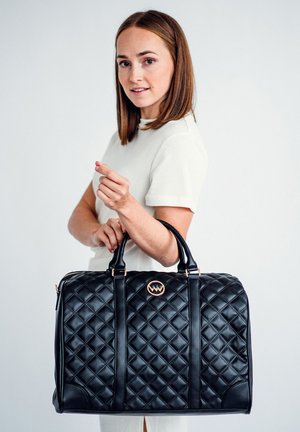 Schwarze, gesteppte Lederhandtasche mit einem strukturierten Design, ausgestattet mit zwei Griffen und einem runden Logo-Akzent auf der Vorderseite.