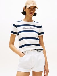 Camisa branca de manga curta com riscas azuis-marinho e o texto "Tommy Hilfiger". Combinada com calções brancos e um boné de basebol em bege claro.