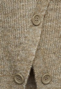 Gros plan sur un tissu beige tricoté présentant trois boutons marron clair à quatre trous alignés verticalement.