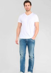 T-shirt blanc en coton à col en V associé à un jean droit bleu clair, avec un design classique à cinq poches et des accents délavés.