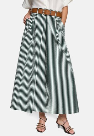 Pantalon à jambes larges à rayures verticales noires et blanches, ceinture marron, mains dans les poches, associé à des talons noirs à brides.