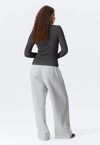 Μαύρο ριμπ μακρυμάνικο τοπ με λευκές κάθετες ρίγες, σε συνδυασμό με φαρδιά γκρι φόρμα. Εστίαση στην πίσω όψη, που δείχνει τις υφές.