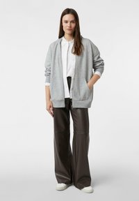 Szara bluza na zamek z luźnym krojem, zestawiona z czarnymi, luźnymi spodniami ze skóry i białymi tenisówkami. Prosty, casualowy design.