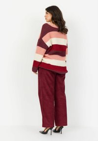 Oversized sweter z wyrazistymi paskami w kolorach różowym, czerwonym i kremowym; połączony z bordowymi spodniami z sztruksu i czarnymi szpilkami.