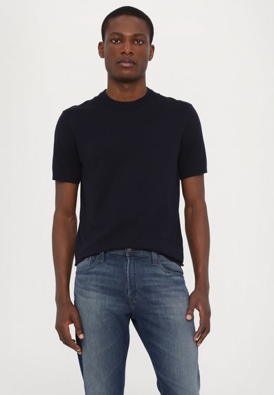 Marineblauwe t-shirt met korte mouwen en ronde hals, gemaakt van zachte stof, gecombineerd met lichtblauwe slim-fit jeans, die een gladde textuur en casual pasvorm laten zien.