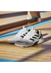 Białe buty sportowe z czarnymi paskami, teksturowana siateczka górna, wyściełany kołnierz i gumowa podeszwa. Lekka konstrukcja odpowiednia do aktywności sportowych.