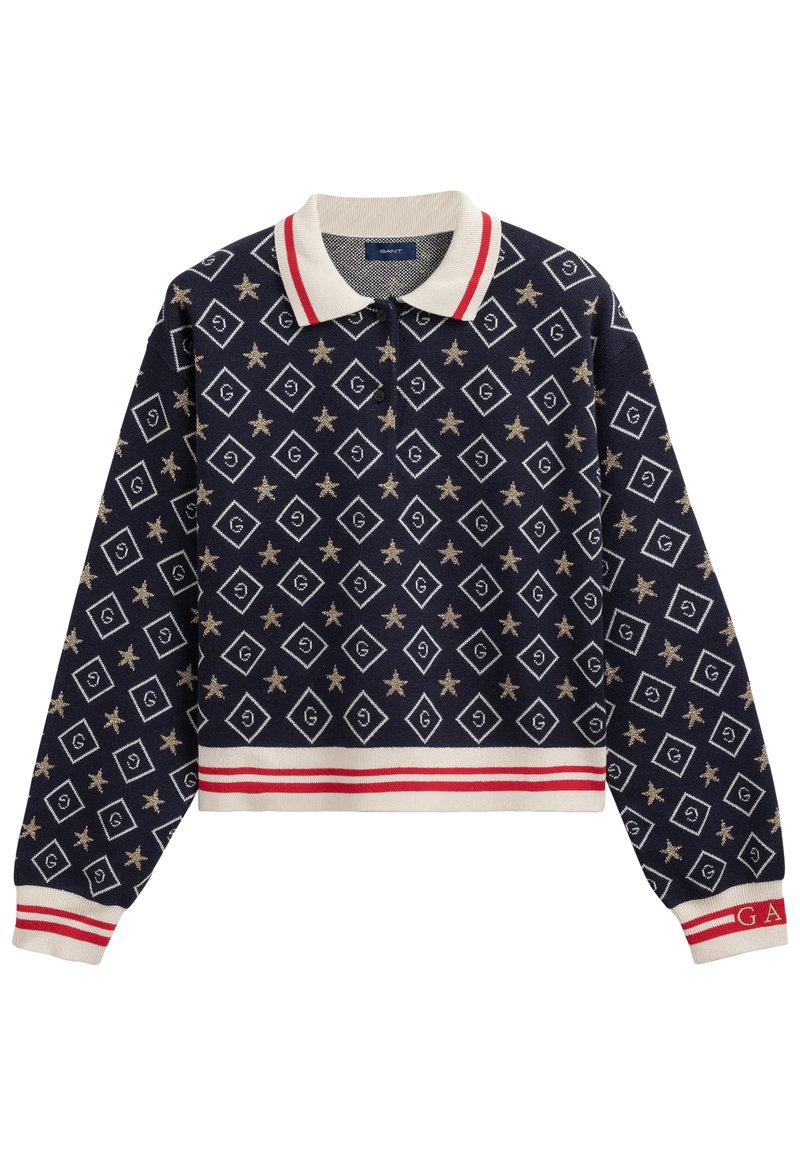 Granatowy krótki pulower z kołnierzykiem polo, zdobiony wzorem w diamenty i gwiazdy w złotym kolorze. Czerwono-białe paski na dolnej krawędzi i mankietach.